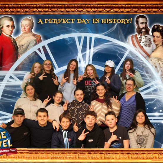 Eine Gruppe von Menschen posiert für ein Foto vor einem historischen Hintergrund mit Porträts und dem Text 'Ein perfekter Tag in der Geschichte!' oben. Das Foto ist in einem goldenen Rahmen.