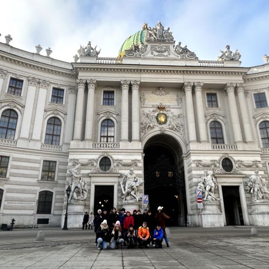 Eine Gruppe von Menschen posiert vor dem Hofburg-Palast in Wien mit Statuen und komplizierten architektonischen Details.