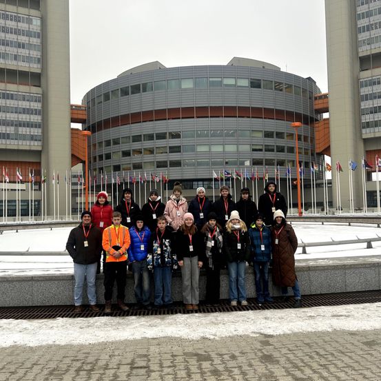 Eine Gruppe von Menschen steht vor einem Gebäude mit Flaggen und Schnee auf dem Boden.