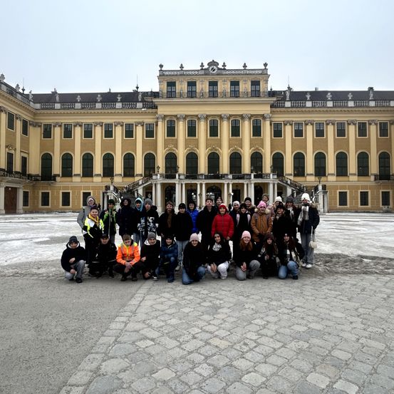 Eine Gruppe von Menschen in Winterkleidung posiert für ein Foto vor einem großen historischen Gebäude.