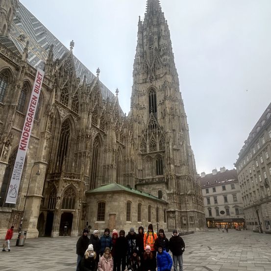 Eine Gruppe von Menschen in Winterkleidung posiert für ein Foto vor dem Stephansdom. Der Dom hat einen großen Turm und eine aufwendige gotische Architektur.
