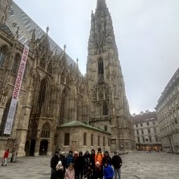 Eine Gruppe von Menschen in Winterkleidung posiert für ein Foto vor dem Stephansdom. Der Dom hat einen großen Turm und eine aufwendige gotische Architektur.
