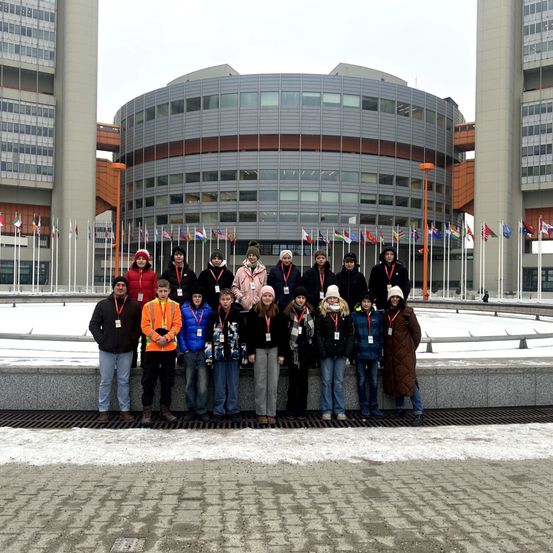 Eine Gruppe von Schülern steht im Winter vor einem modernen Gebäude mit Flaggen und posiert für ein Foto.