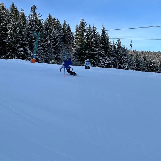 Ein Skifahrer gleitet einen schneebedeckten Hang hinunter, mit Bäumen, die in Schnee gehüllt sind, und einer Skilift im Hintergrund.
