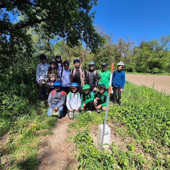 Eine Gruppe von Kindern und Erwachsenen, die Helme und Jacken tragen, posiert für ein Foto auf einem Grasfeld.