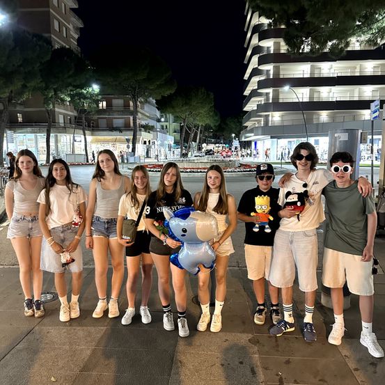 Eine Gruppe junger Leute steht in einer Reihe vor einem Gebäude bei Nacht, einige mit Brille und halten Gegenstände.