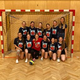Eine Gruppe von Mädchen in blauen Trikots mit dem Buchstaben S und Zahlen posiert für ein Foto vor einem Fußballtor.