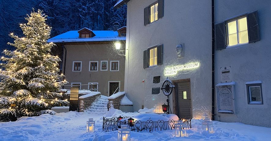 Ein beleuchteter Weihnachtsbaum steht vor einem schneebedeckten Museum. Mehrere Laternen sind entzündet.
