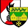 Das Wappen zeigt ein Haus mit Fenstern und einem Kreuz auf einem Schild. Darauf befindet sich ein Zweig mit Tannenzapfen. Auf der linken Seite ist ein rotes und weißes Muster zu sehen.