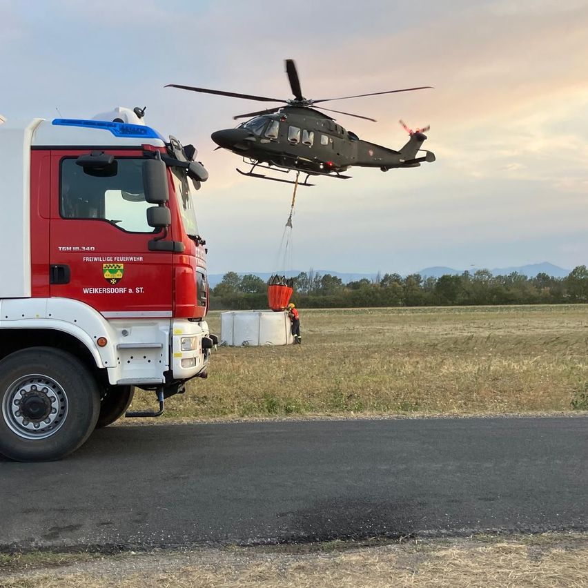 A helicopter is lowering a container to a fire truck on a road. The container is red and white.