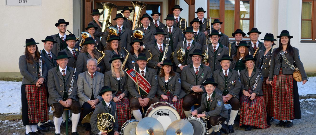 Eine Gruppe von Musikern in traditioneller deutscher Kleidung posiert mit ihren Instrumenten vor einem Gebäude für ein Foto.