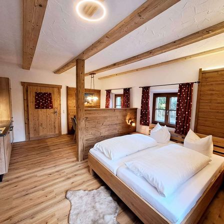 Ein gemütliches Schlafzimmer mit Holzböden und -wänden. Zwei Einzelbetten mit weißen Kissen sind ordentlich gemacht. Der Raum hat ein warmes, rustikales Gefühl mit Holzbalken und einem Teppich.