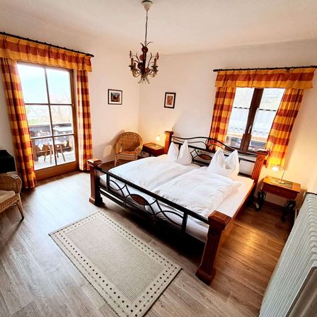 Ein Schlafzimmer mit einem Bett, zwei Nachttischen, einer Lampe und Vorhängen. Das Zimmer hat Holzböden und einen Balkon.