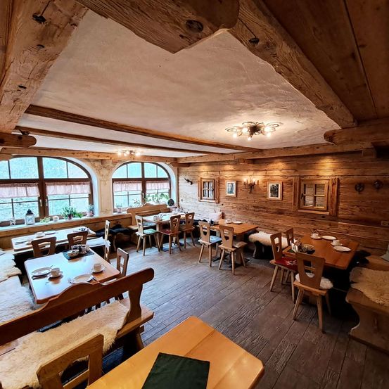 Ein Restaurant mit Holzverkleidung, Tischen und Stühlen, ausgestattet mit Fenstern, Holzbalken und Deckenleuchten. Dekoriert mit Bilderrahmen und einer Kronleuchter.