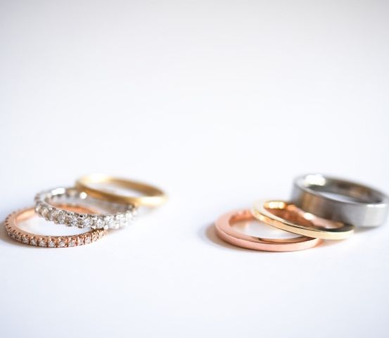 Vier Hochzeitsringe in verschiedenen Farben und Designs auf einer weißen Oberfläche.