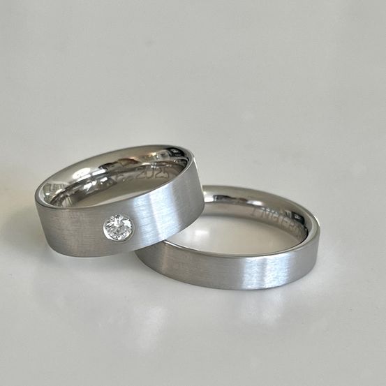 Zwei silberne Ringe mit einem Diamanten auf einem liegen auf einer weißen Oberfläche. Die Ringe haben eine glänzende Oberfläche.