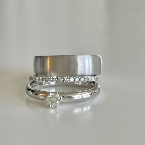 Ein Set aus silbernen Eheringen mit einem Diamanten in der Mitte, auf einer weißen Oberfläche platziert. Die Ringe sind poliert und glänzend.