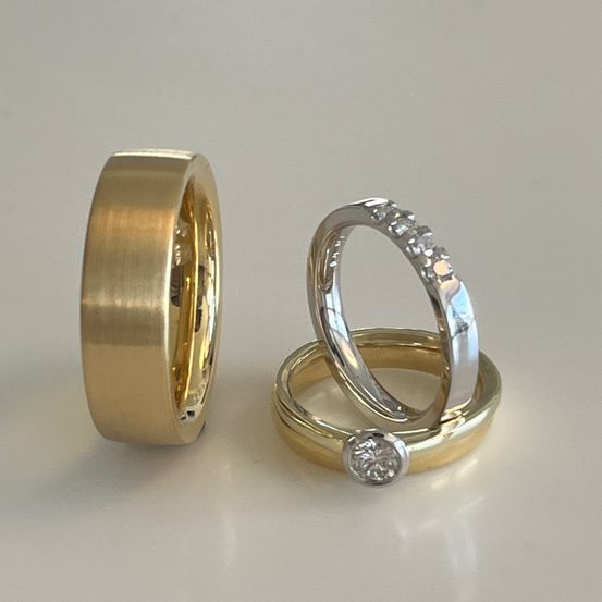 Zwei Ringe, einer aus Gold und einer aus Silber, sind ausgestellt. Der Goldring hat eine glatte, polierte Oberfläche. Der Silberring ist mit kleinen Diamanten verziert.