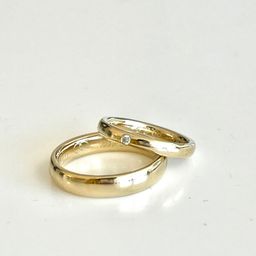 Zwei goldene Eheringe auf weißem Hintergrund, einer mit einem kleinen Diamanten.