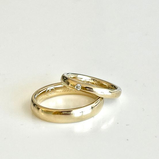 Zwei goldene Eheringe auf weißem Hintergrund, einer mit einem kleinen Diamanten.