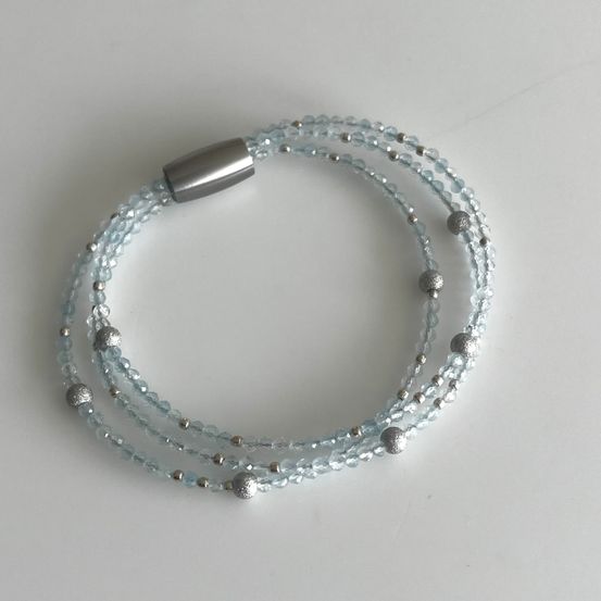 Ein hellblaues Armband mit mehreren Strängen, Silberperlen und einer Silberverschluss auf einer weißen Oberfläche.
