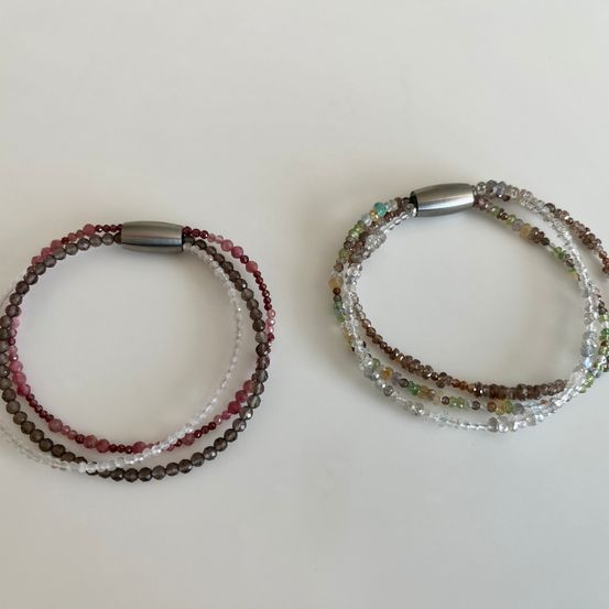 Zwei Armbänder mit verschiedenen Farben und Kristallperlen liegen auf einer weißen Oberfläche. Jedes Armband hat eine silberne Schließe.