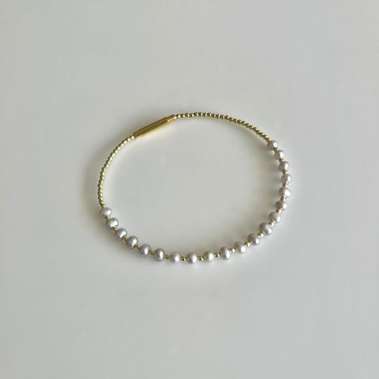 Ein goldenes Armband mit Perlen auf weißem Hintergrund. Die Perlen sind in einer Reihe angeordnet und an einer goldenen Schließe befestigt.