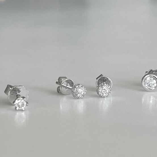 Vier kleine Silber-Ohrstecker mit Diamantsteinen, auf einer weißen Oberfläche platziert.