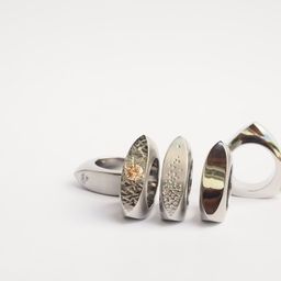 Eine Sammlung von Silberringen mit einzigartigen Designs auf weißem Hintergrund. Ein Ring hat einen gelben Edelstein.
