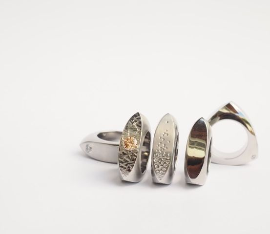 Eine Sammlung von Silberringen mit einzigartigen Designs auf weißem Hintergrund. Ein Ring hat einen gelben Edelstein.