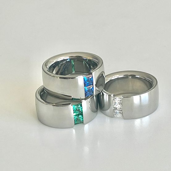 Drei silberne Ringe gestapelt, jeder mit unterschiedlichen Edelsteinen: einer mit blauem, einer mit grünem und einer mit Diamant.