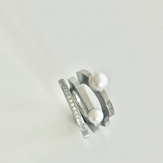 Ein silberner Ring mit zwei weißen Perlen und Diamantakzenten auf weißem Hintergrund.