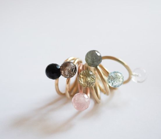 Ein goldener Ring mit mehreren kleinen Edelsteinperlen, darunter schwarze, rosa, grüne und durchsichtige Steine, vor weißem Hintergrund.