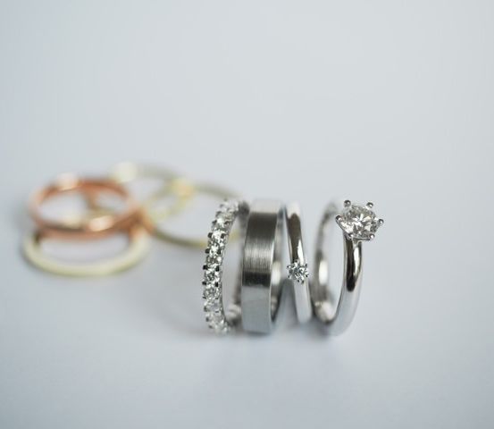 Fünf Ringe, darunter zwei mit Diamanten, liegen auf einer weißen Oberfläche. Die Ringe unterscheiden sich in Farbe und Design.