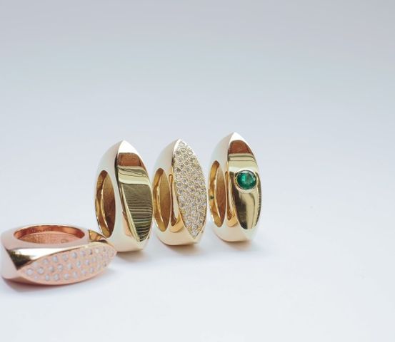 Eine Sammlung von Goldringen mit verschiedenen Verzierungen, einschließlich Diamanten und einem grünen Edelstein auf weißem Hintergrund.