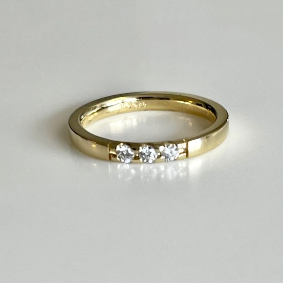 Ein Goldring mit drei kleinen Diamanten in einer Reihe auf einer weißen Oberfläche.