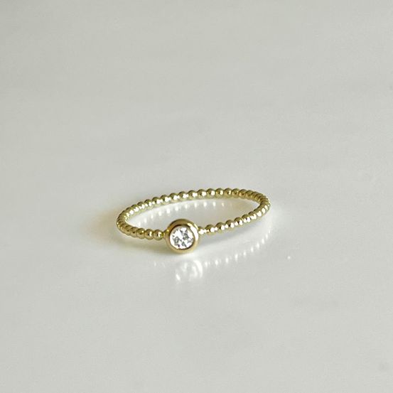 Ein goldener Ring mit kleinen weißen Diamanten in der Mitte wird auf einem weißen Hintergrund präsentiert.