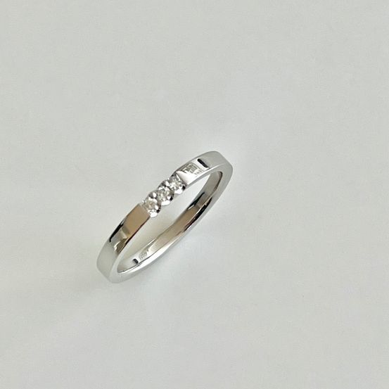 Ein Silberring mit drei kleinen Diamanten in der Mitte. Der Ring hat eine polierte Oberfläche.