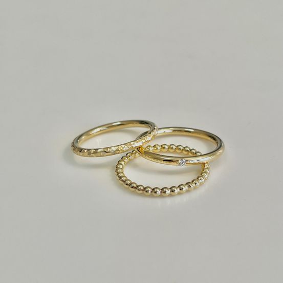 Drei goldene Ringe mit feinen Mustern, einer mit einem kleinen Diamanten, ordentlich auf einem weißen Hintergrund angeordnet.