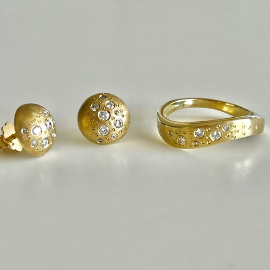 Drei goldene Schmuckstücke mit Diamanteinlagen auf weißem Hintergrund. Ein Ring, ein kleiner runder Ohrstecker und ein größerer runder Ohrstecker.