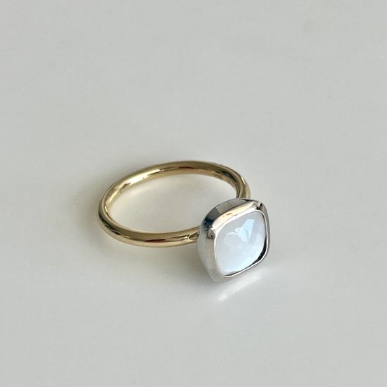 Ein goldener Ring mit einem weißen quadratischen Stein in einer silbernen Fassung. Der Stein ist leuchtend.
