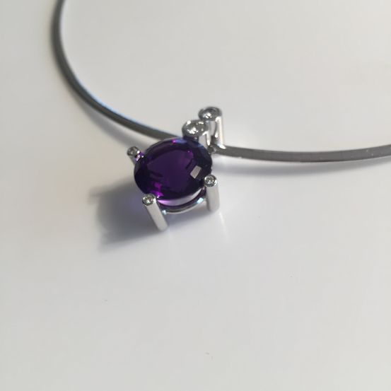 Eine Silberkette mit einem zentralen violetten Edelstein und kleinen Diamanten darum herum, die auf einer weißen Oberfläche ruht.