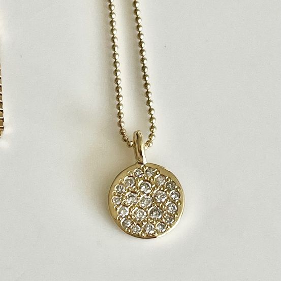 Eine goldene Halskette mit einem kreisförmigen Anhänger, verziert mit vielen kleinen Diamanten, auf weißem Hintergrund.