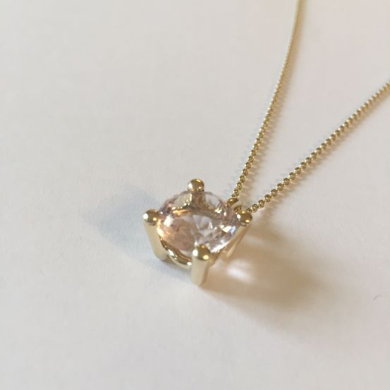 Eine goldene Halskette mit einem runden, rosa Edelstein-Anhänger auf weißem Hintergrund.