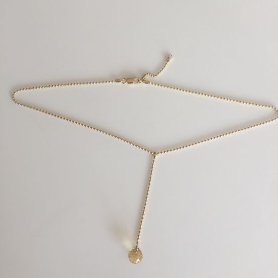 Eine goldene Halskette mit einem runden Anhänger hängt auf weißem Hintergrund. Die Kette besteht aus einer Perlenkette und einem kleinen runden Anhänger.
