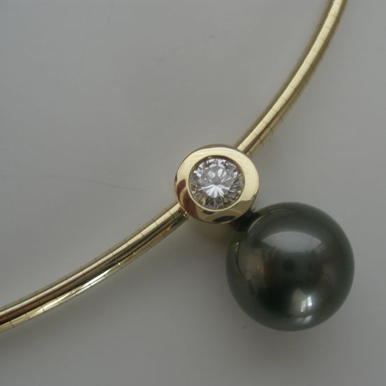 Eine goldene Halskette mit Diamantanhänger und großem schwarzen Perlmuttperle auf weißem Hintergrund.