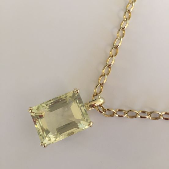 Eine Goldkette mit einem gelben, rechteckigen Edelstein-Anhänger. Der Anhänger hat einen quadratischen Schliff und ist in einem Goldverschluss gefasst.