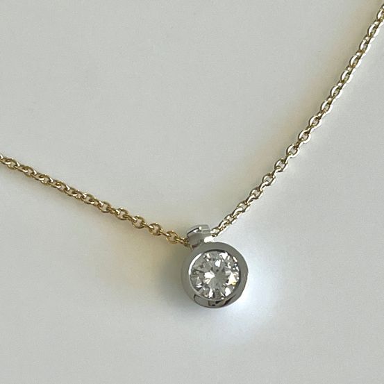 Eine goldene Kette mit einem runden Anhänger, der einen einzelnen Diamanten hält, auf einer weißen Oberfläche gezeigt.