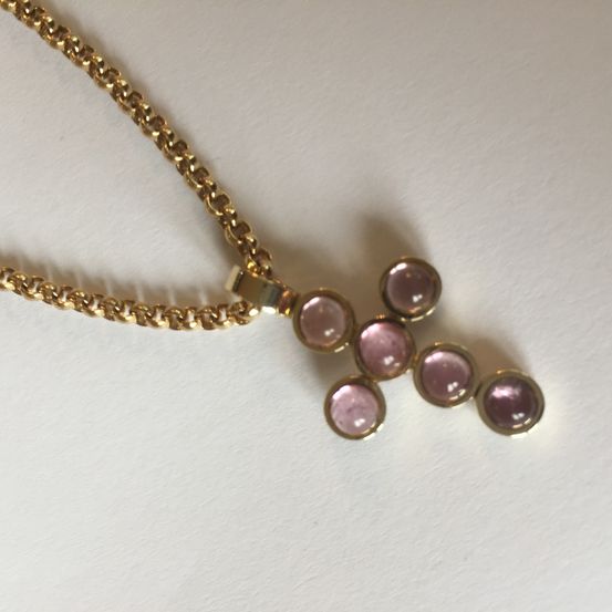 Eine Goldkette mit fünf rosa Edelsteinen wird auf einer weißen Oberfläche präsentiert.