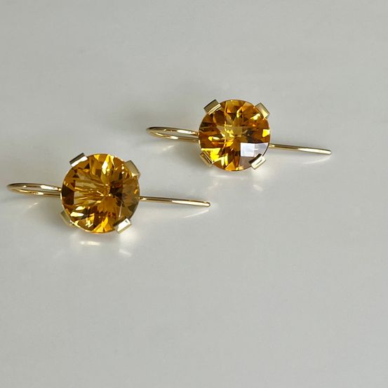 Zwei goldplattierte Ohrringe mit großen, runden, gelb-orangefarbenen Citrin-Steinen. Die Steine sind in einem runden Goldrahmen gefasst, und die Ohrringe haben einen goldenen Stift an der Rückseite.